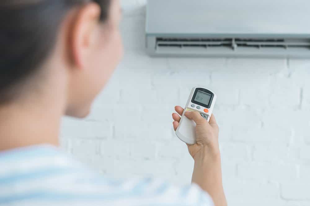 A person points a remote control at a wall-mounted ductless AC, ideal air conditioning for apartments.