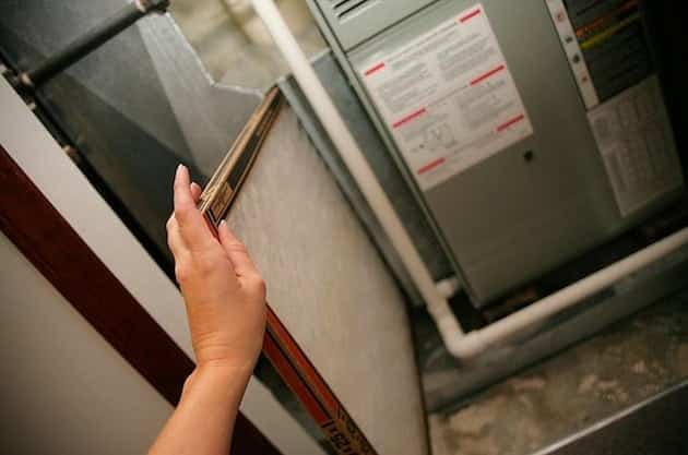 A person's hand holding an air filter being placed into a furnace unit.
