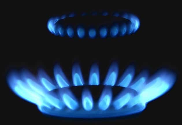 Close-up of two blue natural gas flames burning in the dark, featuring the distinctive circular pattern of a lit stove burner.