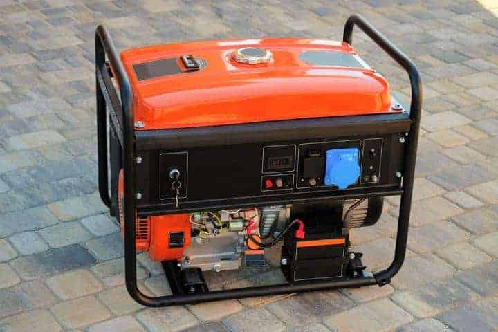 An orange portable generator with a black front panel featuring various controls and an outlet, resting on a stone-paved surface.
