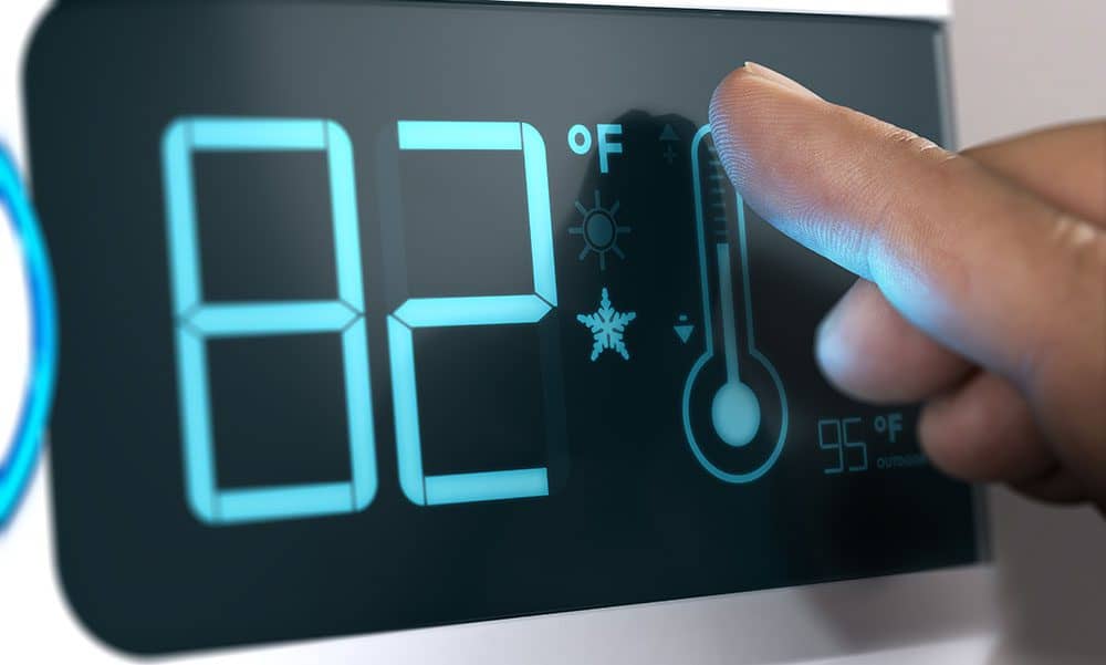 A finger adjusts the temperature on a digital thermostat set to 82°F, featuring icons for heat, cool, and outdoor temperature at 95°F.