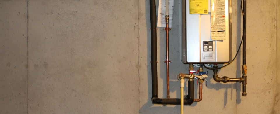 A tankless water heater mounted on a concrete wall with pipes and valves connected.