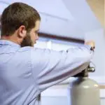 Person in a blue shirt adjusting the valve on a large gray tank indoors.