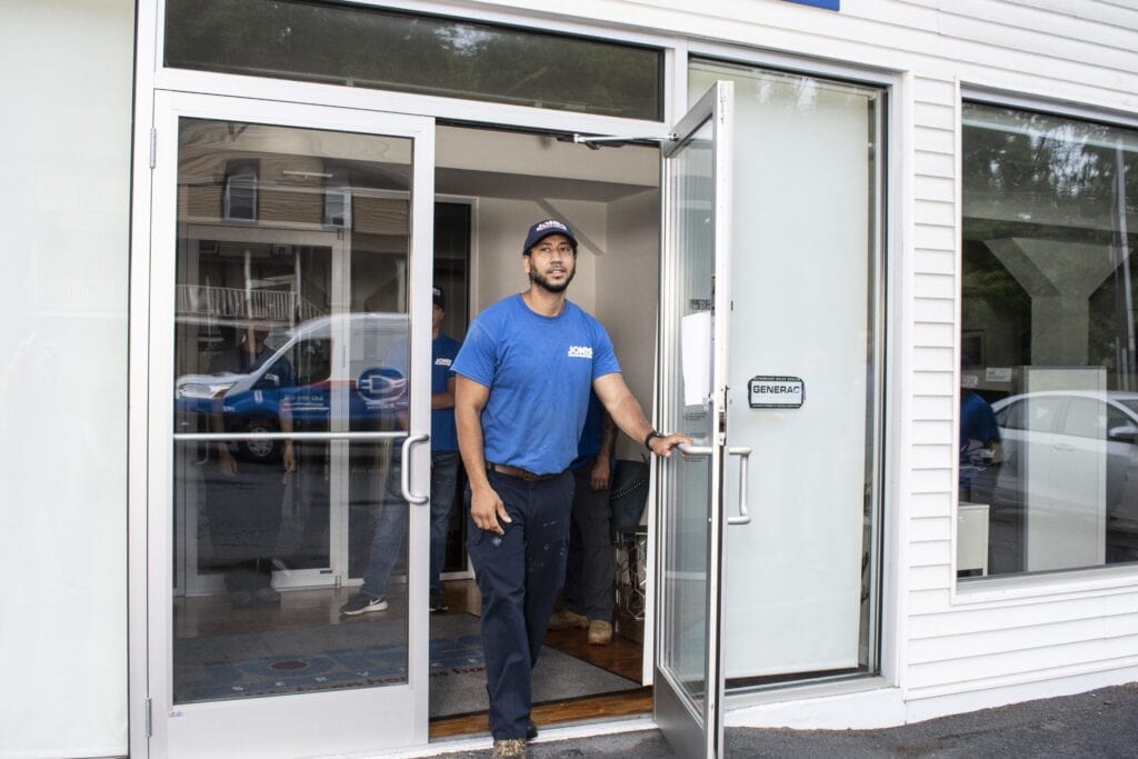 A man wearing a blue shirt and cap opens a glass door of a building. A van is visible through the glass.