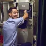 Person smiling while servicing a furnace in a utility room.