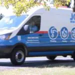 White and blue service van with symbols for plumbing, heating, cooling, and electrical services parked on a sunny day.