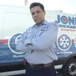 Person in a work uniform stands with arms crossed in front of a service van with business branding.