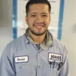 Smiling person wearing a work uniform with name tag reading "Xavier," standing indoors.