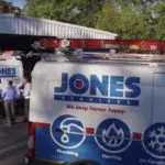 Jones Services vans parked outside a building, with logos indicating plumbing, heating, and air services. People stand nearby.