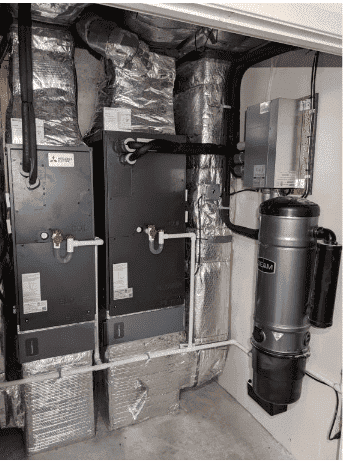 Industrial HVAC system with metal ducts, insulated pipes, and a central vacuum unit mounted on the wall in a utility room.