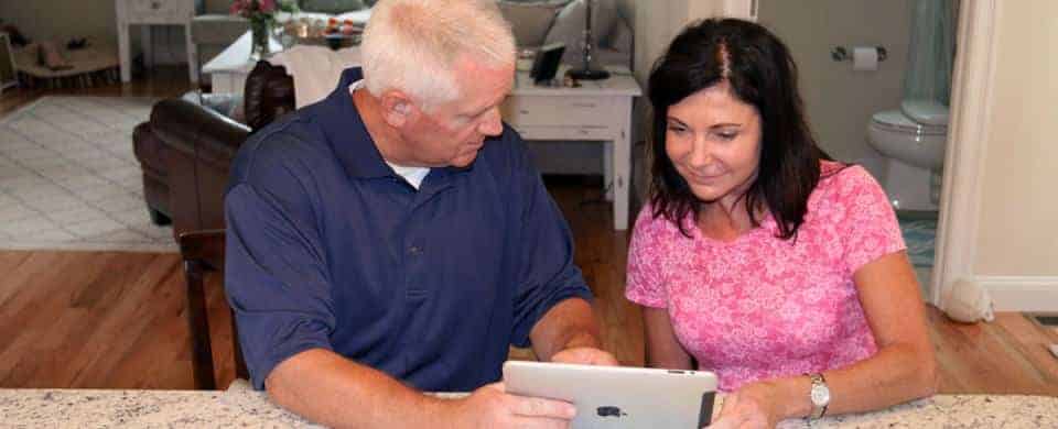 A man and a woman sit at a table looking at a tablet device together in a home setting.