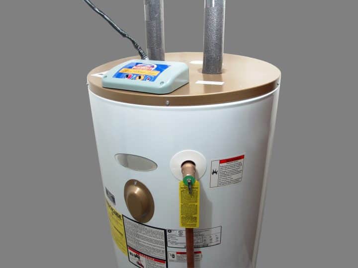 A white cylindrical water heater with metal pipes, a digital control panel, and various informational labels and warnings attached.