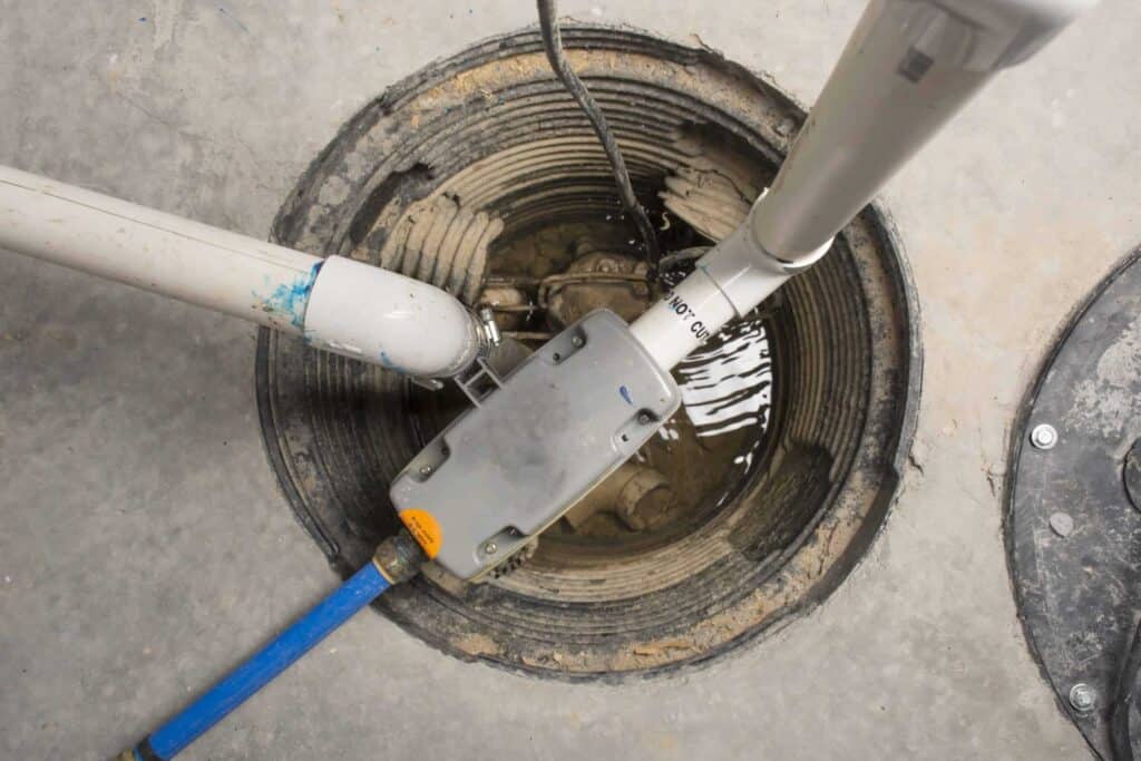 A sump pit with connected pipes and electrical wires, partially filled with water.