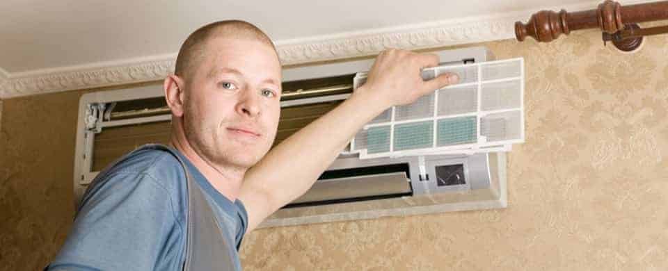 A person changing the filter of a wall-mounted air conditioning unit.