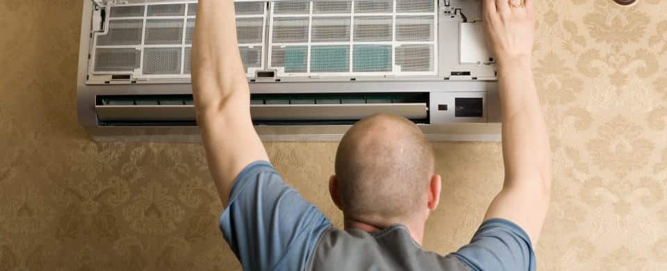 Person adjusting or installing a wall-mounted air conditioning unit indoors.