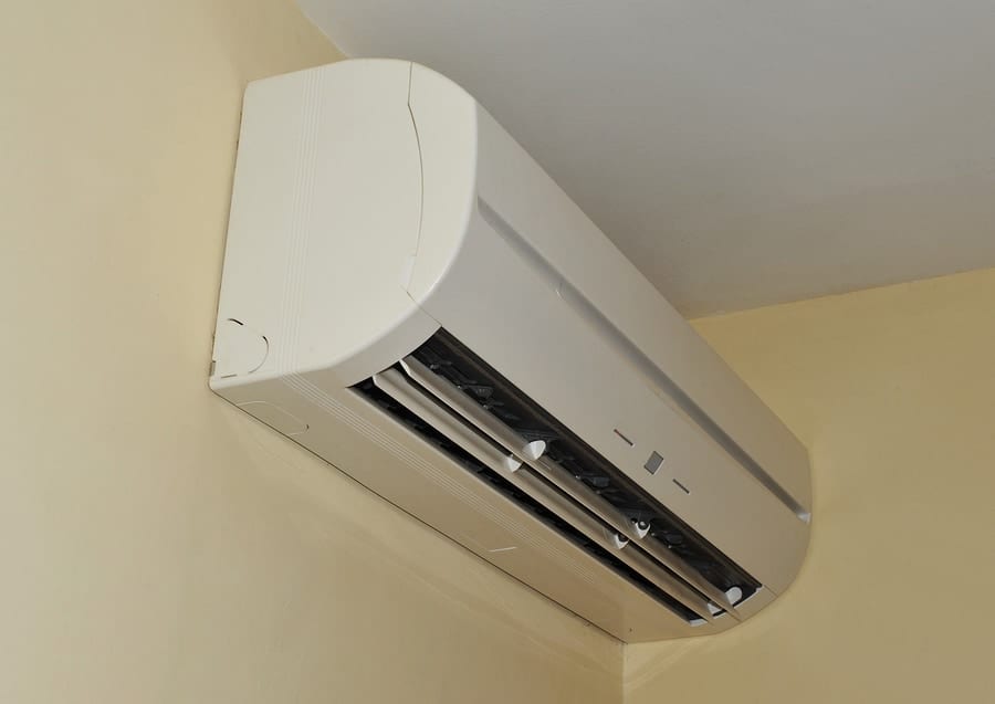 Wall-mounted air conditioning unit installed in the corner of a room with a beige wall.