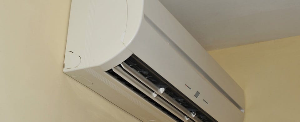 Wall-mounted air conditioning unit installed near the ceiling on a beige wall.