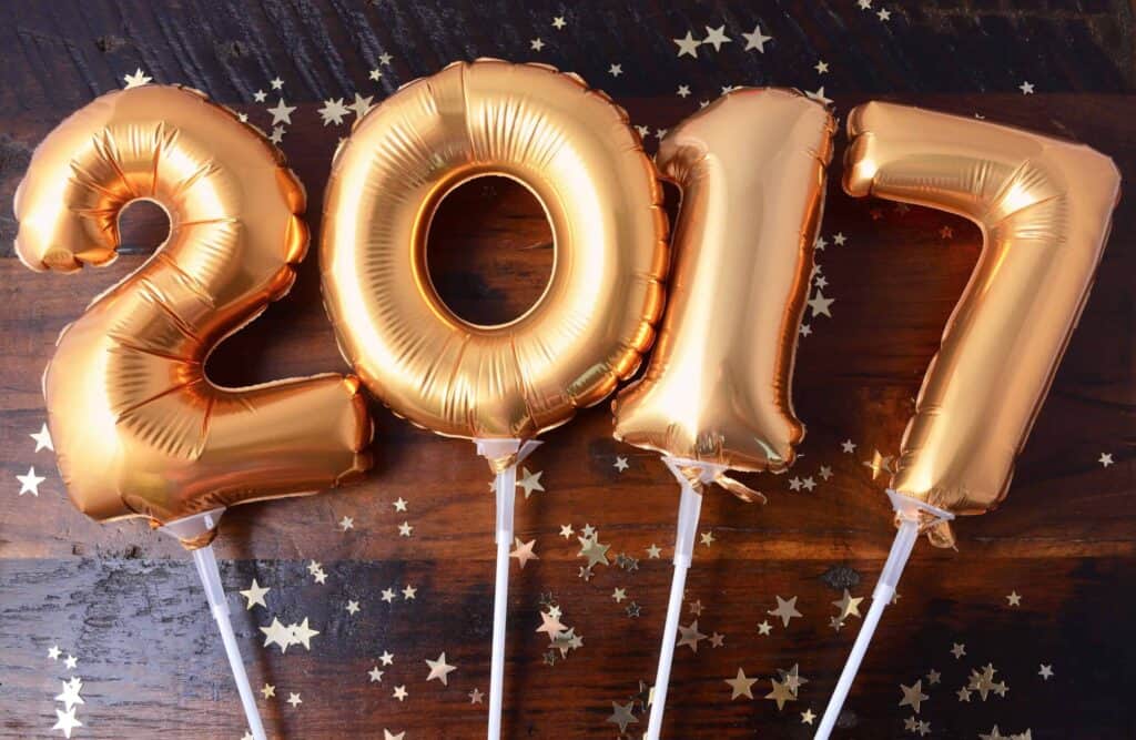 Gold foil balloons displaying "2017" on a wooden surface, surrounded by star-shaped confetti.