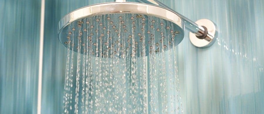 A silver showerhead with water streaming down against a blue tiled background.