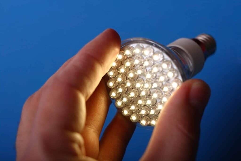 A hand holds an illuminated LED light bulb against a blue background.