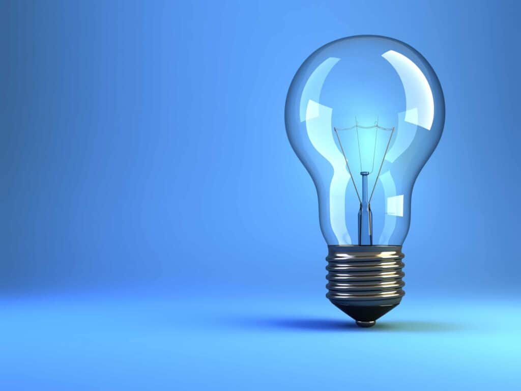 A clear glass light bulb with a metallic base stands upright against a smooth blue background.