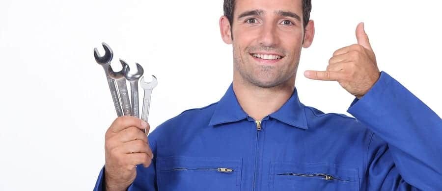 Man in a blue work uniform holds three wrenches and makes a hand gesture.