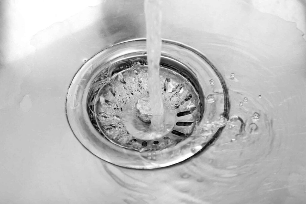 Water flows down a stainless steel sink drain.