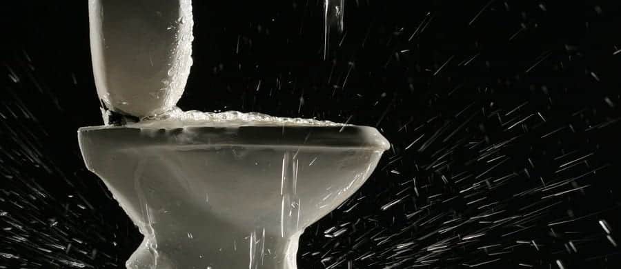 Water overflowing from a toilet, splashing droplets in various directions against a dark background.