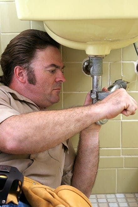 Man repairing pipes under a bathroom sink.
