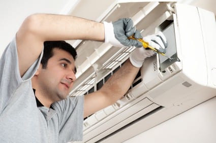 Technician wearing gloves repairing an air conditioning unit with a screwdriver.