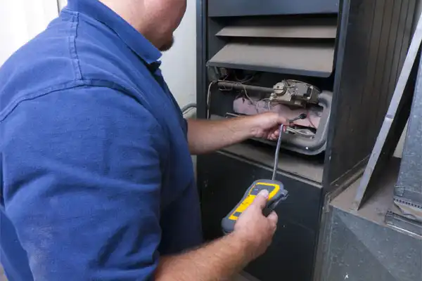 A person in a blue shirt uses tools to inspect and test a furnace, ensuring precision in general heating repair by checking components inside the unit.