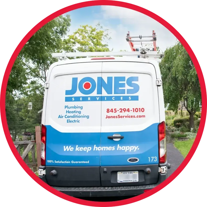 A white Jones Services van is parked on a driveway. The rear doors display the company logo, contact info, and list plumbing, heating, air conditioning, and electric services.