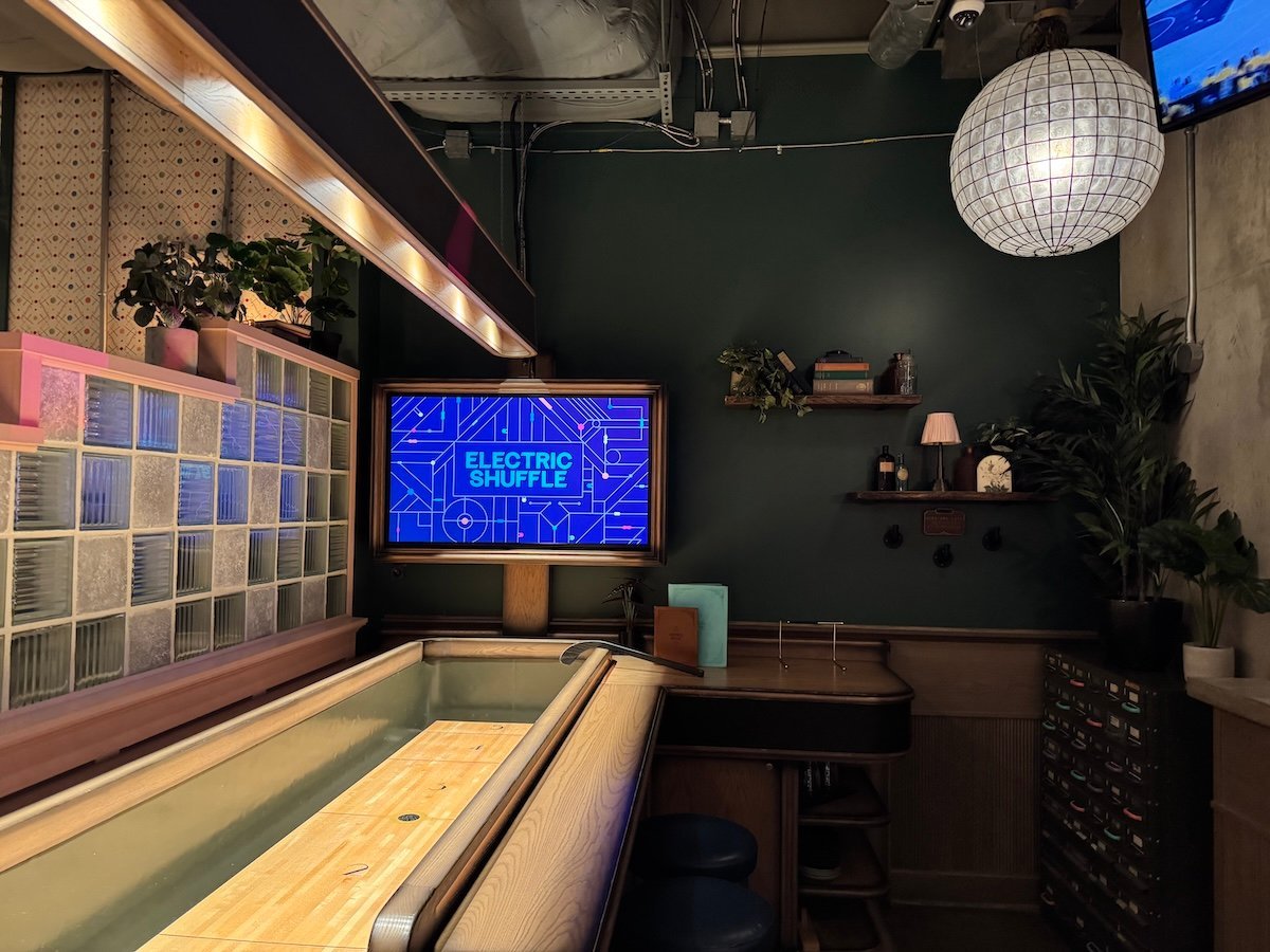 A shuffleboard table, plants, and bookshelves at Electric Shuffle.