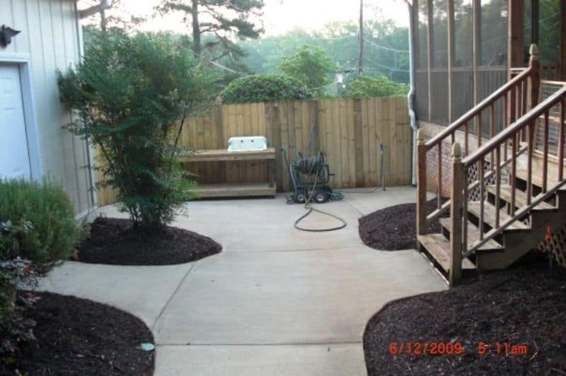 Concrete backyard patio with landscaping, wooden stairs, and garden edging, designed by John Russell Landscape Architect for outdoor living and aesthetic appeal.