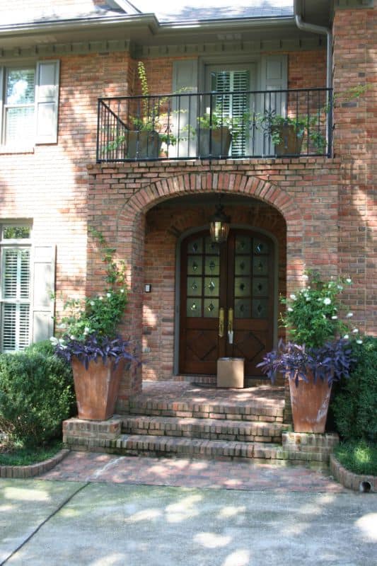 Elegant brick home entrance with lush landscaping, potted plants, and a charming front porch designed by John Russell Landscape Architect.