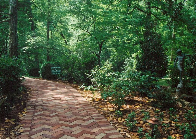 Lush green landscape with brick walkway and garden sculptures by John Russell Landscape Architect. Beautiful natural design emphasizing landscape architecture and outdoor garden planning.