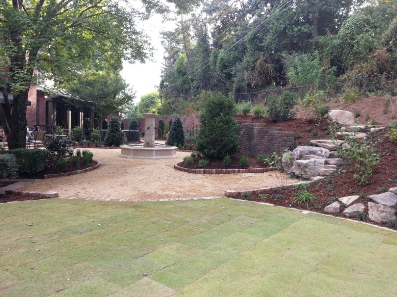 Lush landscaped backyard with stone pathways, decorative shrubs, and a central fountain, designed by John Russell Landscape Architect for an elegant outdoor living space.