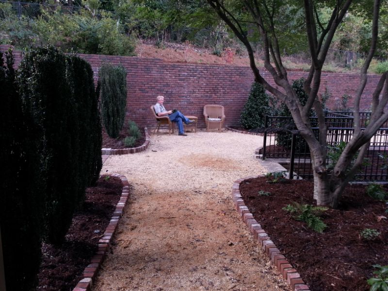 Landscape design by John Russell Landscape Architect with a cozy backyard patio featuring trees, brick edging, and seating areas for outdoor living.