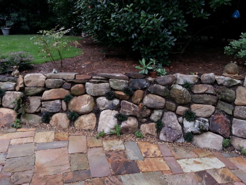 Stunning custom stone retaining wall designed by John Russell Landscape Architect showcasing natural rock masonry and lush garden landscaping.