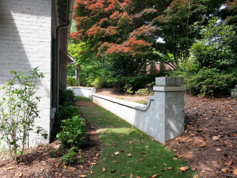 Elegant landscape design by John Russell Landscape Architect featuring a classic brick wall and lush foliage in a serene residential garden.