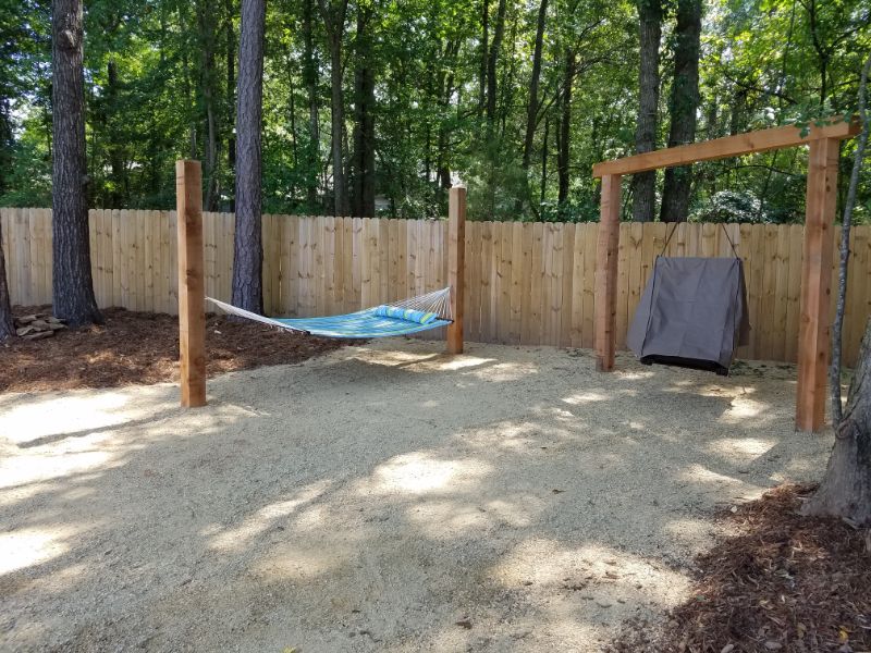 Hammock and outdoor swing set in a backyard space designed by John Russell Landscape Architect, featuring natural wood fencing and shaded woodland environment for relaxation and leisure.