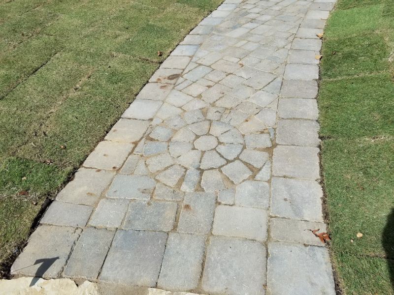 Gray stone paved walkway with circular pattern, landscaped garden path design, outdoor hardscaping by John Russell Landscape Architect, durable patio stones, elegant garden hardscape design, US outdoor landscape solutions.