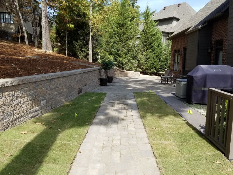 2. Beautiful landscaped backyard with stone walkway, lush green grass, and tall pine trees, designed by John Russell Landscape Architect for outdoor living and aesthetic appeal.