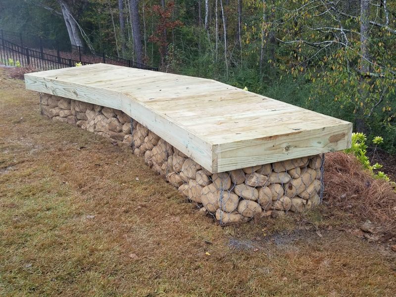 Firewood storage bench with wood and wire mesh base, outdoor landscape design, rustic wood and stone seating, backyard firewood storage solution, John Russell Landscape Architect specialized landscaping design.