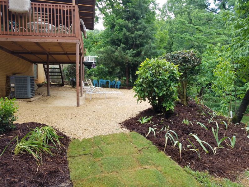 Lush backyard landscape design featuring shrubs, flowering plants, and a tiered elevated deck with seating area by John Russell Landscape Architect.