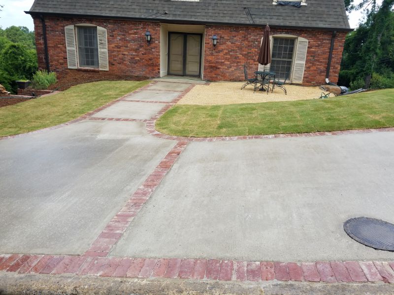Enhanced driveway and walkway with brick edging and landscape design by John Russell Landscape Architect, featuring lush lawn, decorative gravel, and outdoor seating area.