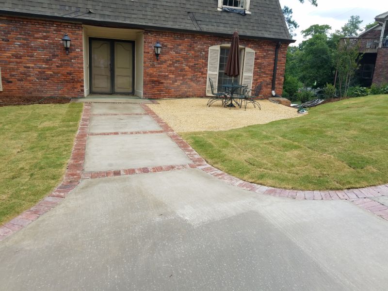 Sophisticated landscape design featuring a brick-bordered concrete walkway leading to a charming brick house entrance.