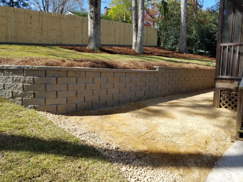 Retaining wall with landscaped garden area, decorative stonework, and mature trees in a backyard, designed by John Russell Landscape Architect, showcasing expert landscape architecture.