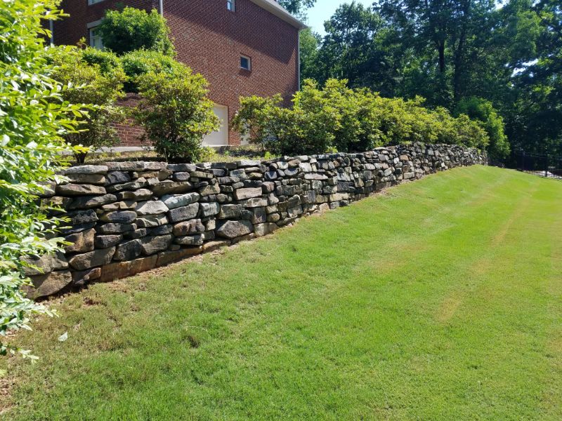 Natural stone retaining wall landscape design with lush greenery and manicured lawn.
