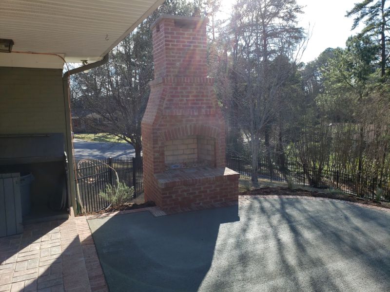 Fireplace design by John Russell Landscape Architect, outdoor brick fireplace in backyard, perfect for outdoor entertaining, surrounded by trees and natural landscape, professional landscape architecture services.